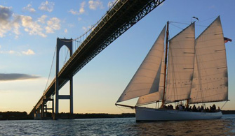 a sailboat cruising down a river, going under a large bridge